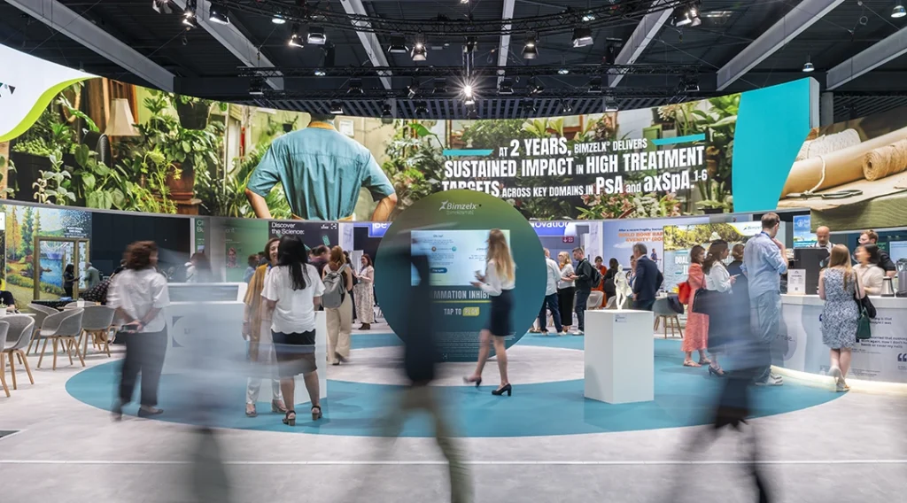 A busy pharmaceutical trade fair in Barcelona, set inside a modern exhibition hall with high ceilings and bright lights.